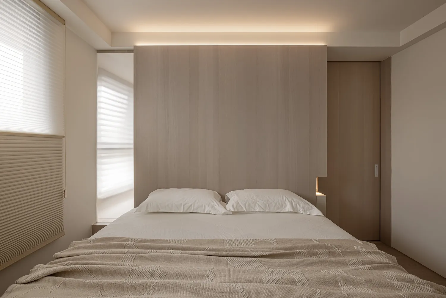 A minimalist bedroom with neutral-toned bedding and a large window allowing natural light to fill the space.
