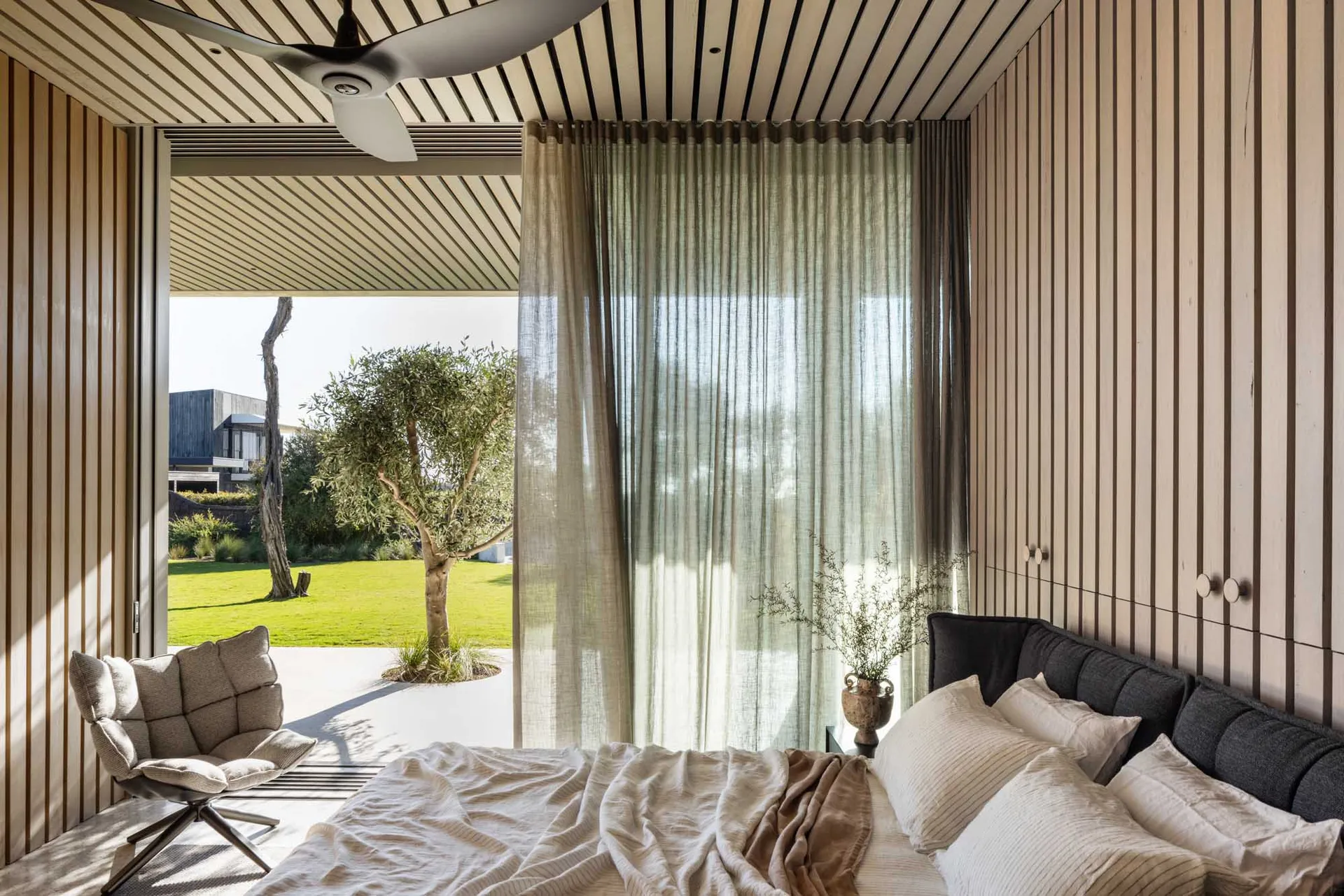 A minimalist bedroom with wooden walls, a bed, and a curtain lets in natural light.