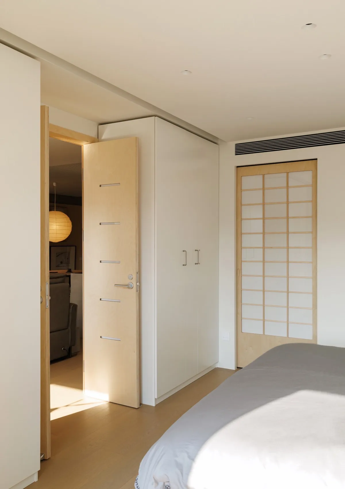 A minimalist bedroom featuring wooden paneling and a bed with white linens.