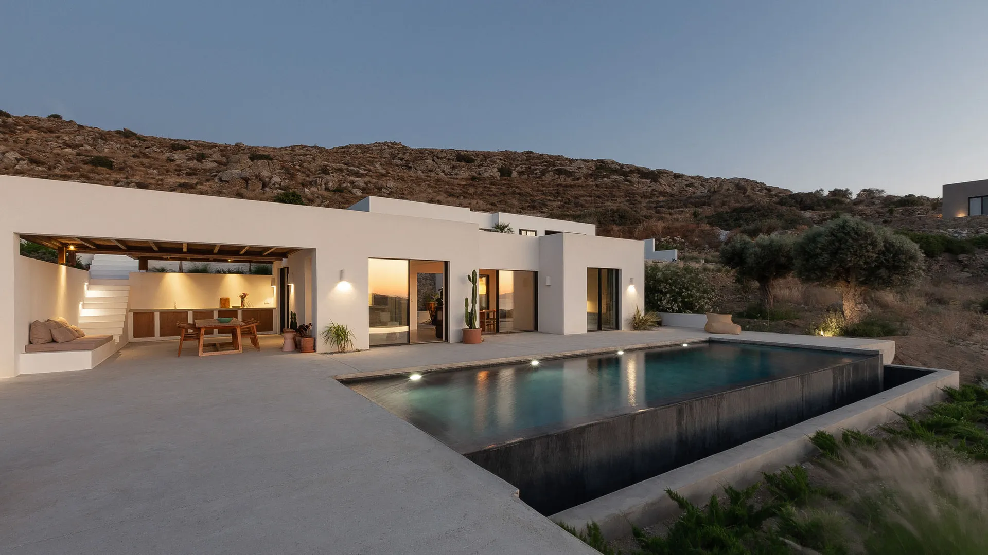 A minimalist villa with a concrete exterior, featuring a modern pool and large windows overlooking the landscape.