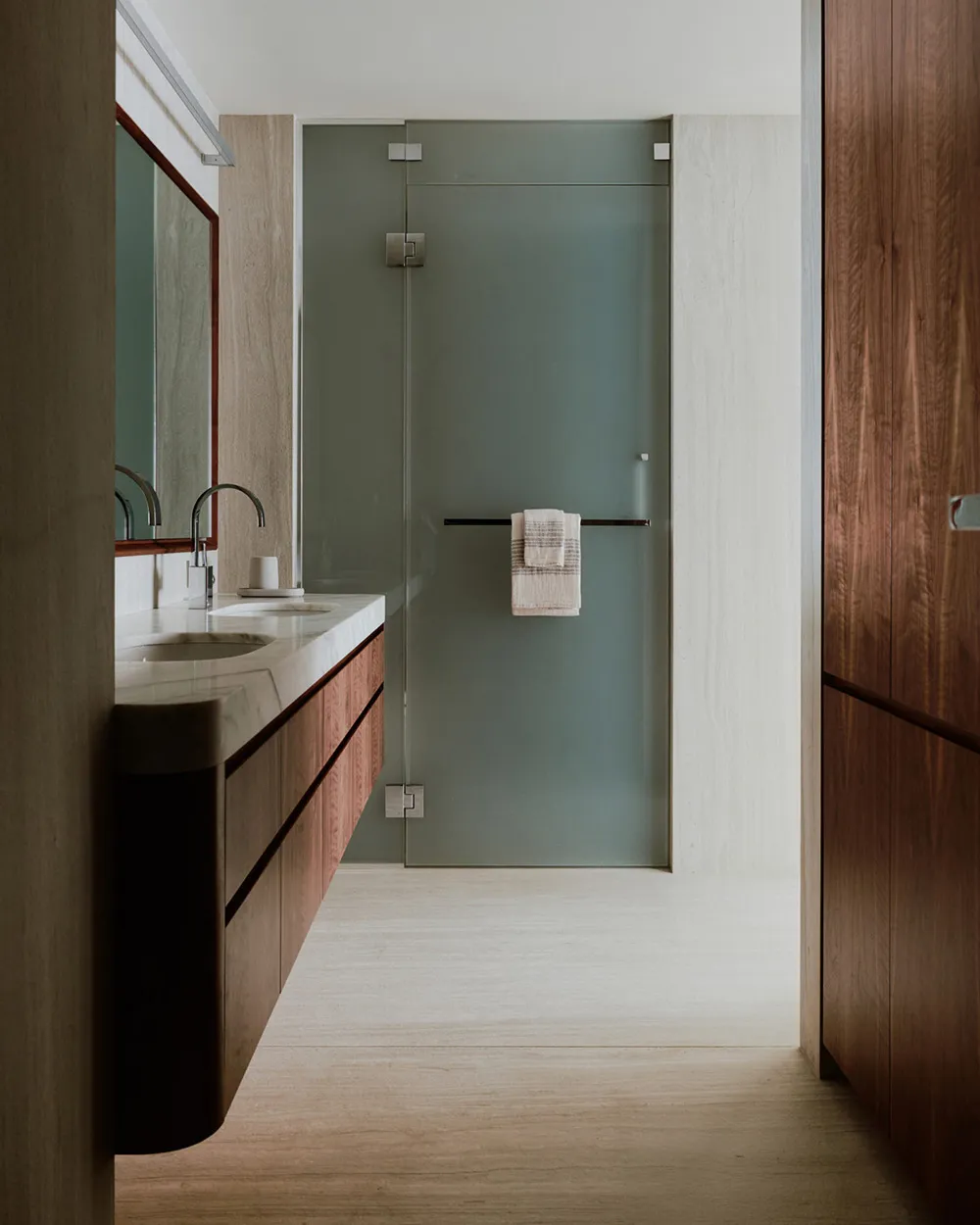 Modern bathroom with glass shower enclosure, wooden cabinets, and white marble countertop.