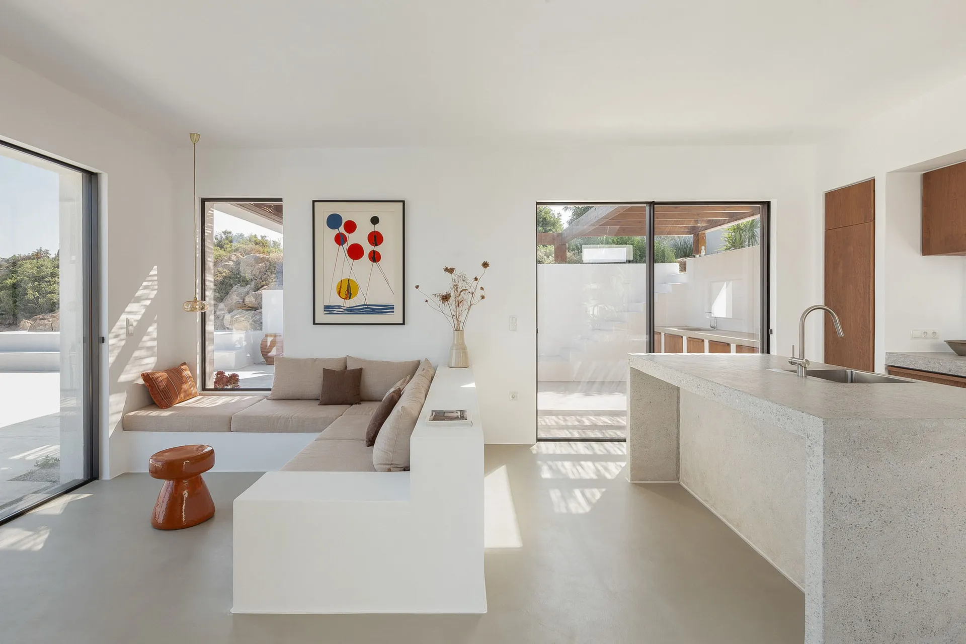 A modern living room with concrete flooring, minimalist furniture, and abstract art on the wall, featuring a built-in bench s