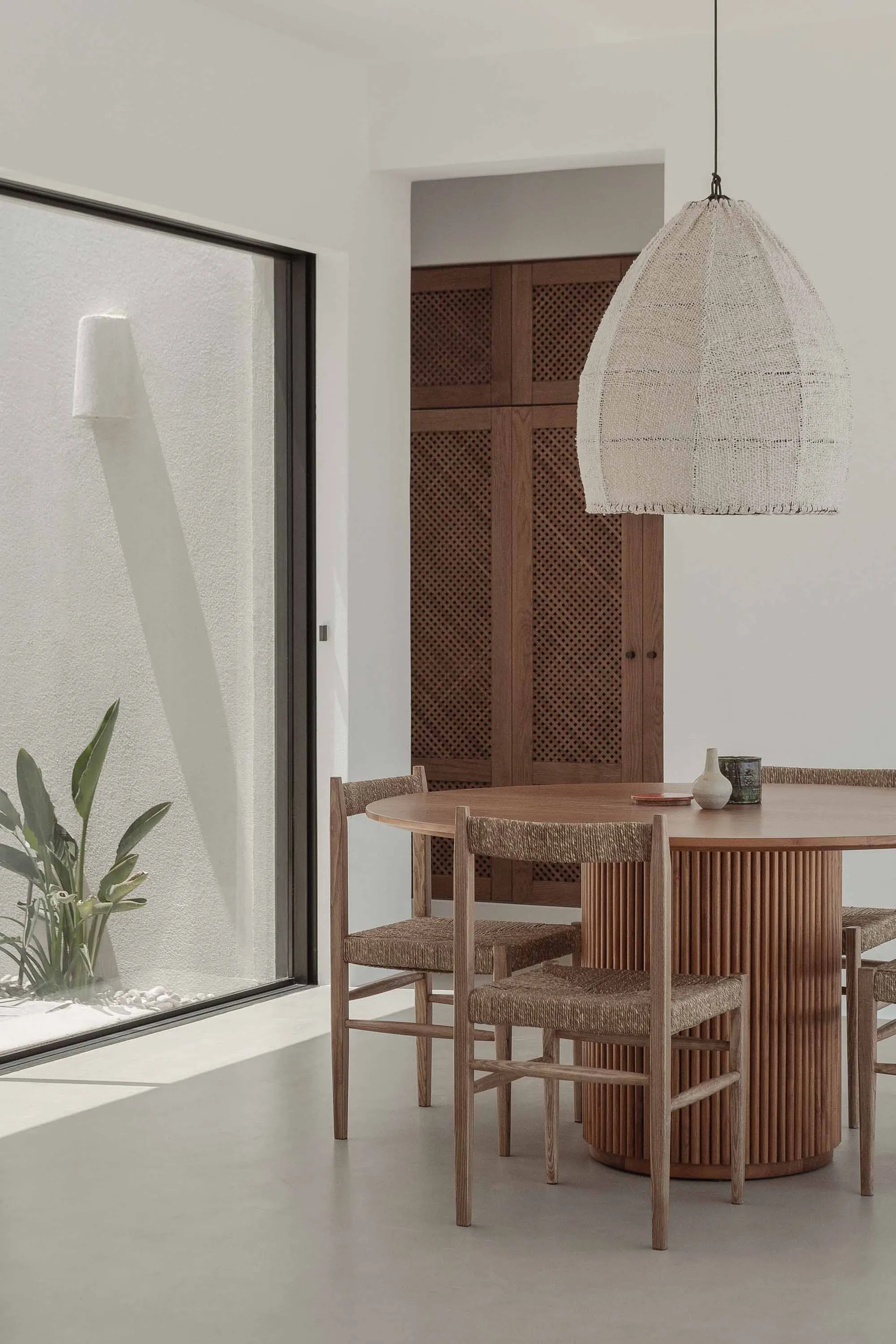 Modern dining room featuring a wooden table with straw-wrapped chairs, natural light from a window with a textured interior w