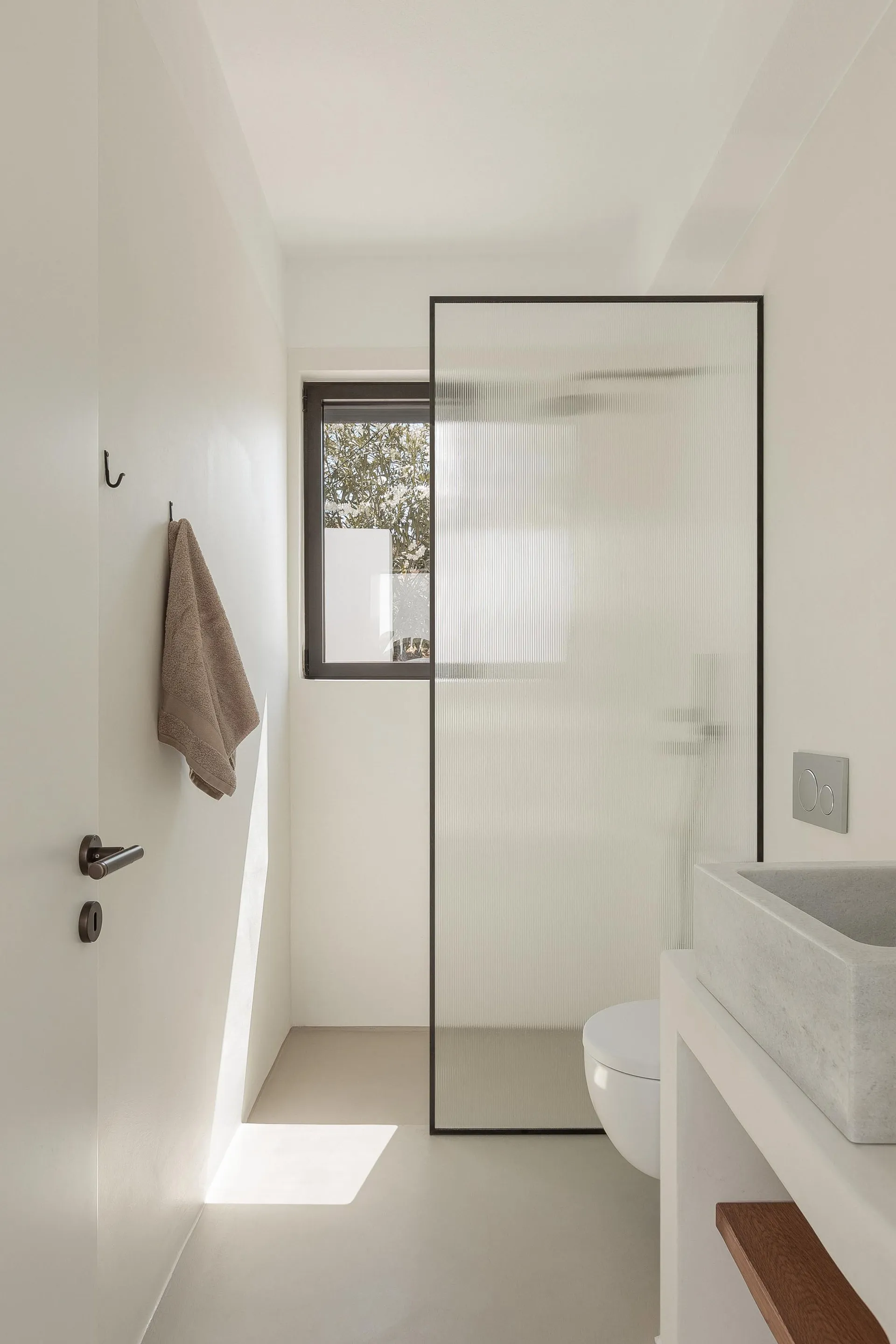 Modern minimalist bathroom with concrete sink, frosted glass shower enclosure, and minimalistic decor.