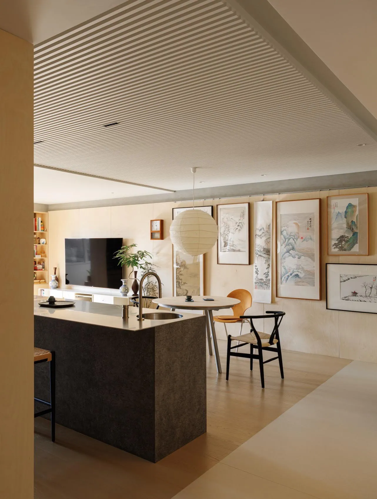 A modern residential living room with minimalist design, featuring a black kitchen island, a round dining table, and framed a