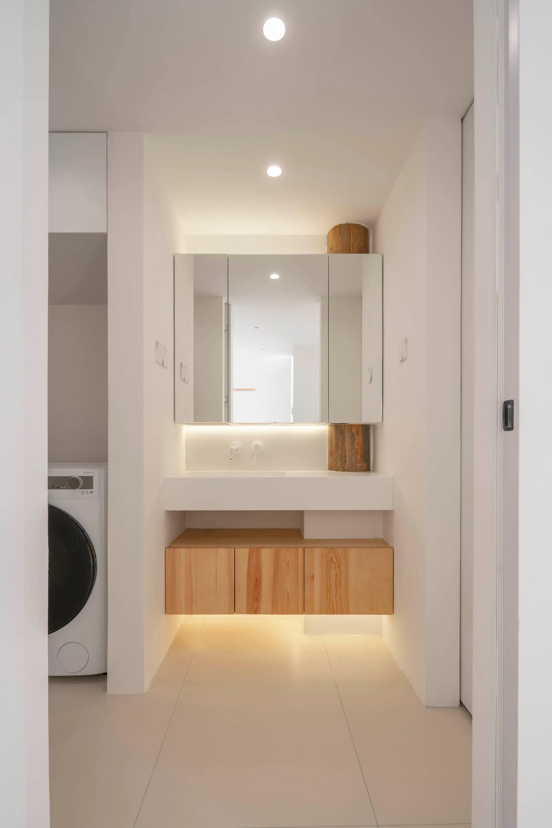 A minimalist bathroom featuring white concrete walls, glass fixtures, and wooden cabinets.