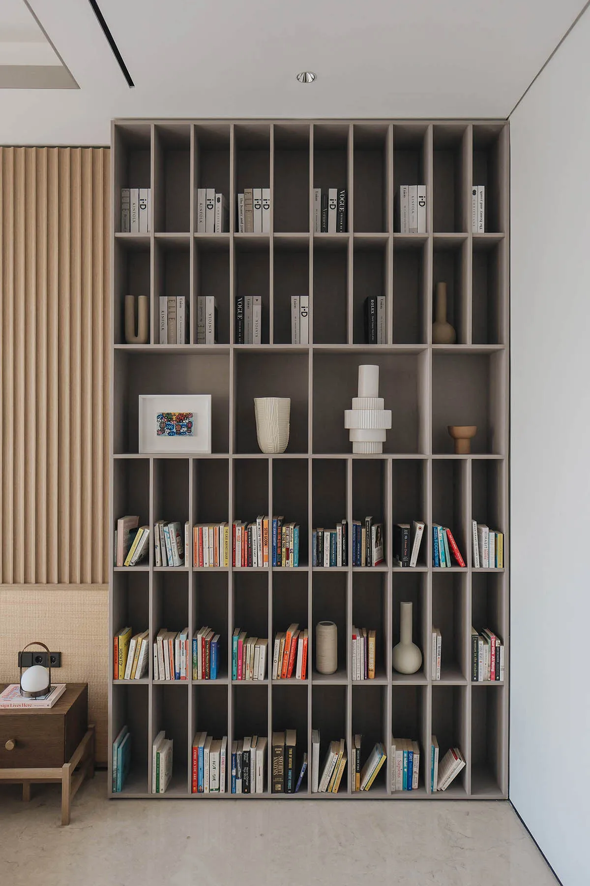 A minimalist bookshelf made of wood, filled with books and decorative vases.