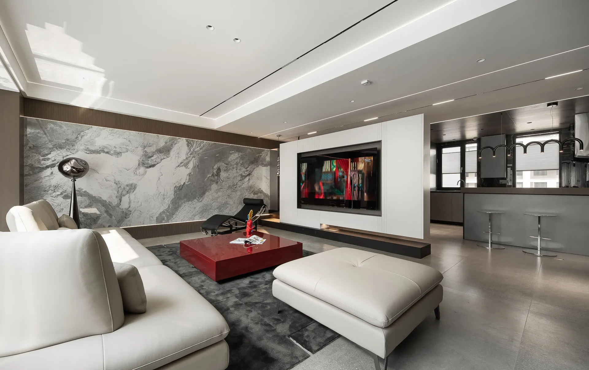 A modern living room with a large granite accent wall, a white sectional sofa, a red coffee table, and a flat-screen TV mount