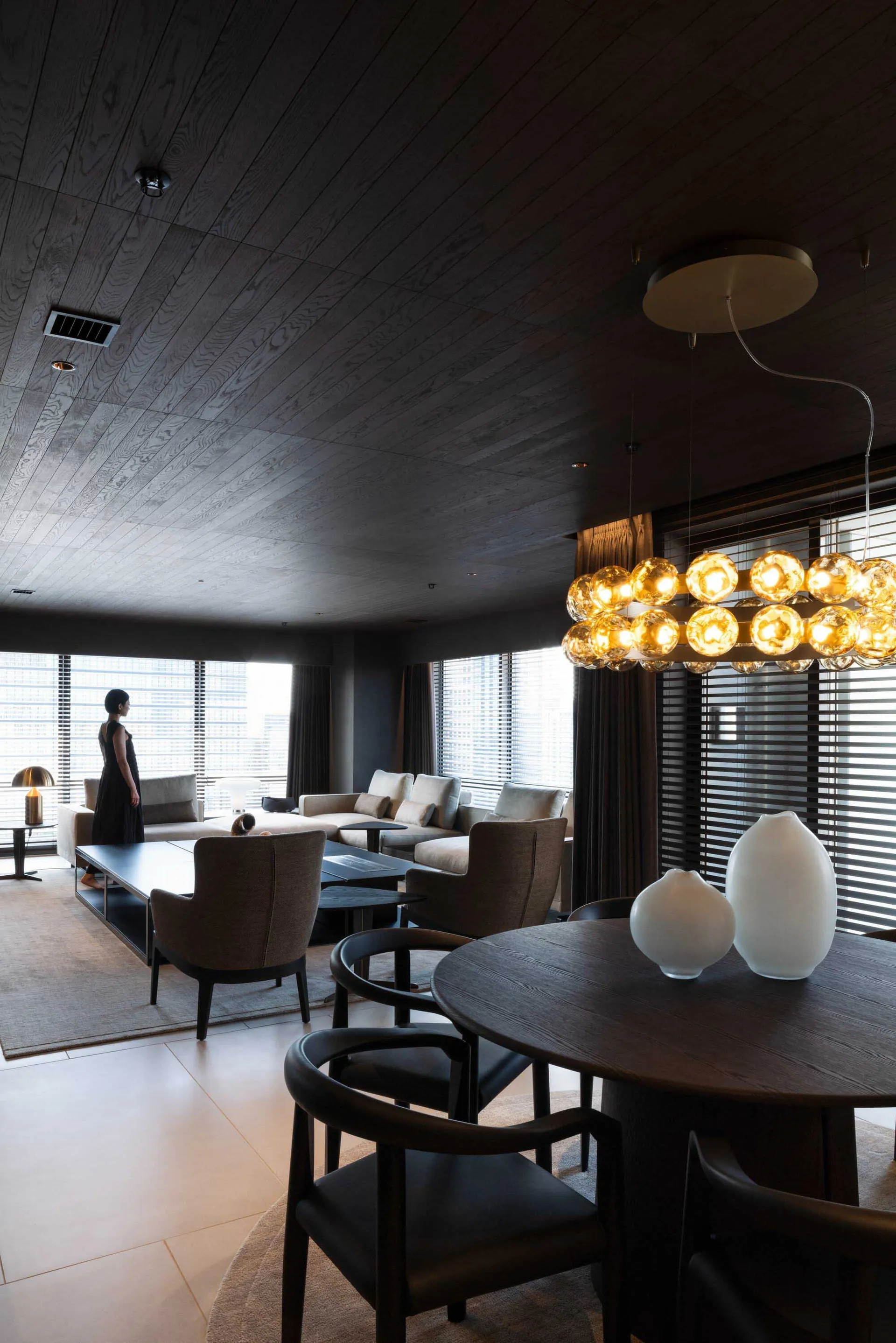 Modern living room with black walls, wooden floor, and industrial chandelier.