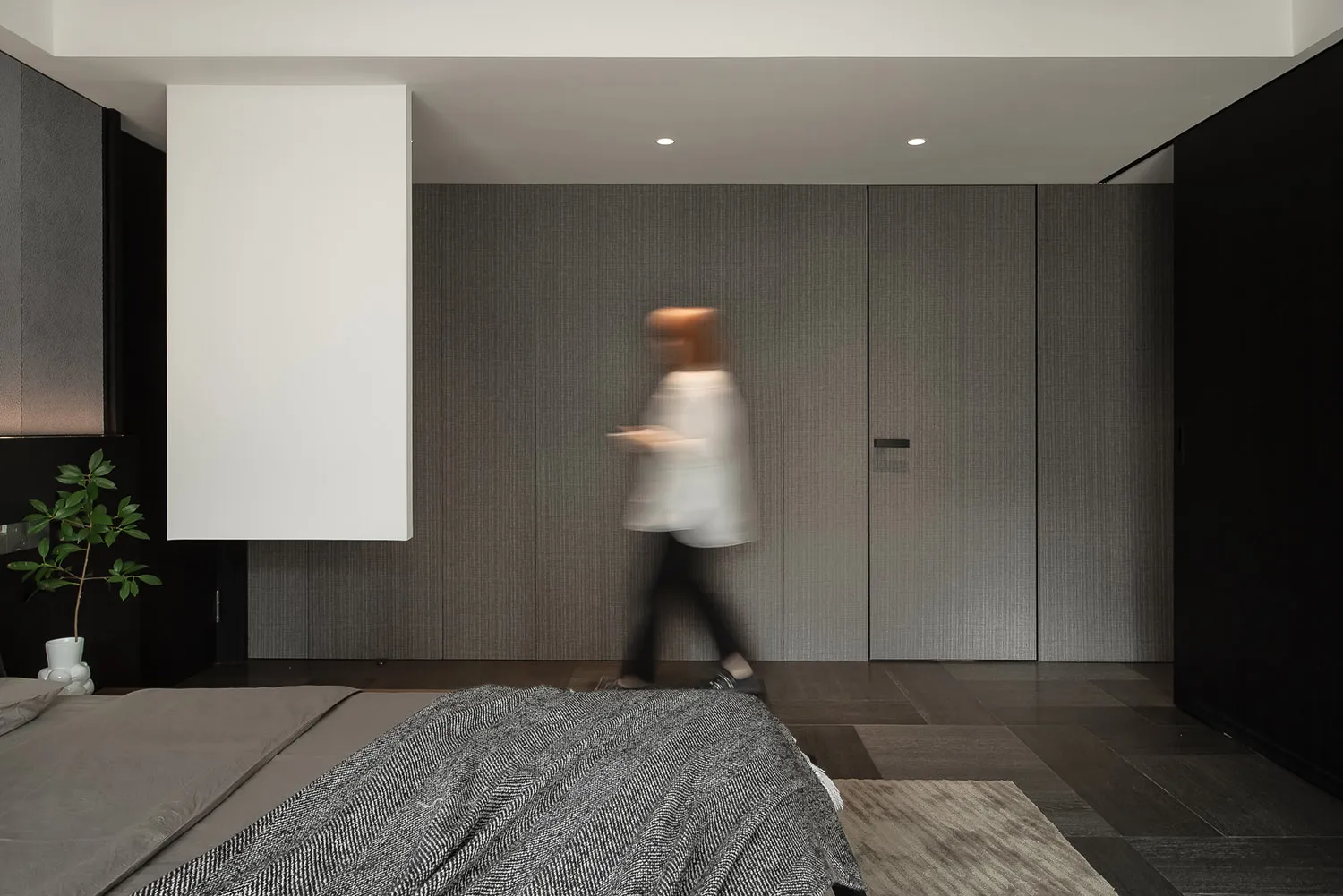 A minimalist bedroom featuring dark tones, a textured wall, and a bed with a patterned blanket.