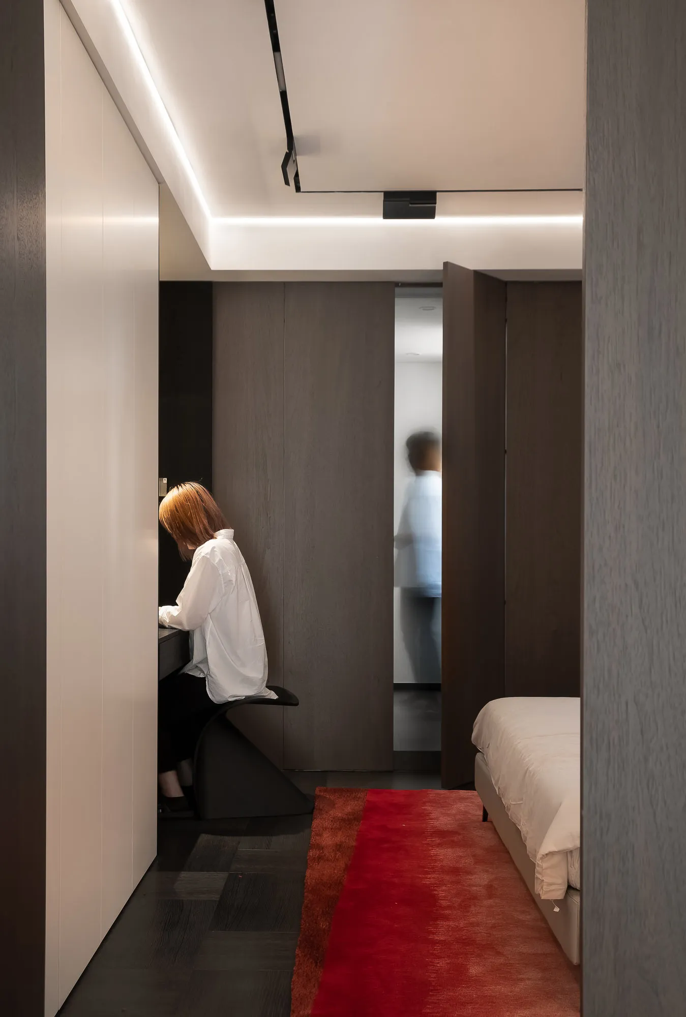 A minimalist bedroom featuring wood cabinets, metal accents, and a red carpet.