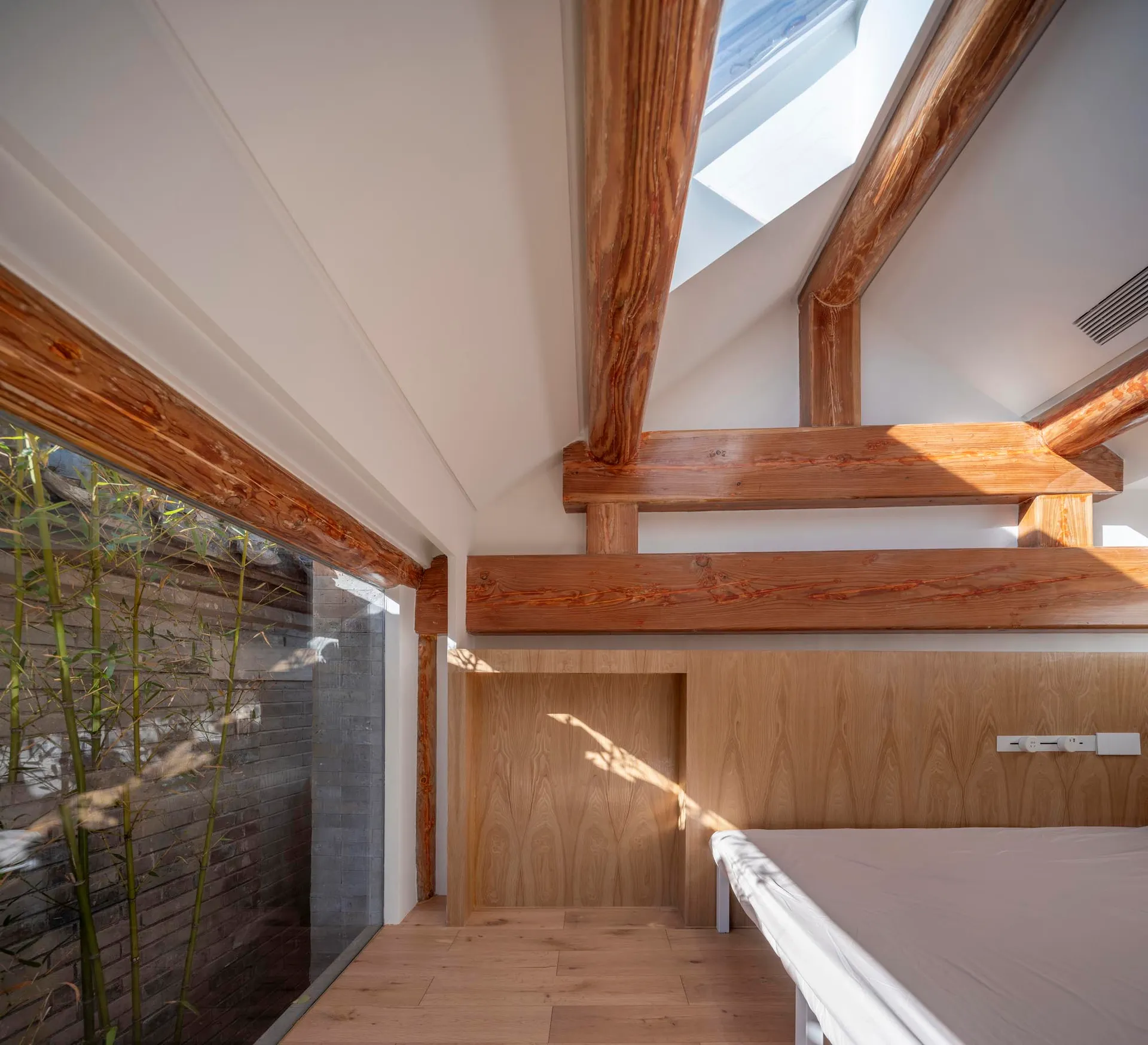 A modern minimalist bedroom featuring wooden beams and a skylight.