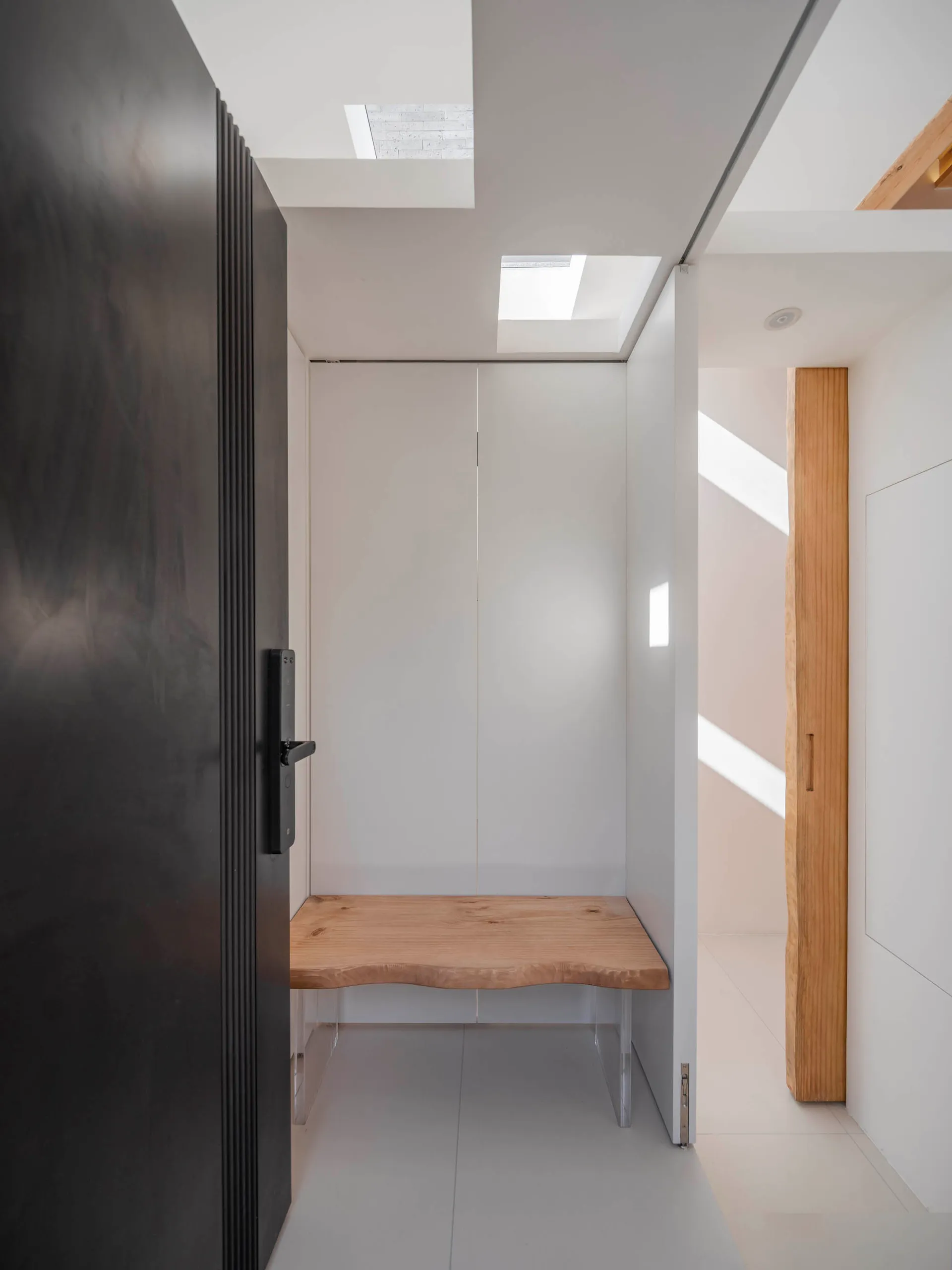 Modern minimalist entryway featuring a wooden bench and steel door with large glass panels.