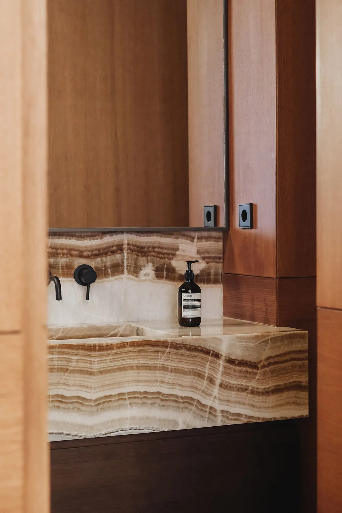 A minimalist bathroom with a marble countertop, black fixtures, and a bottle of Aesop lotion.