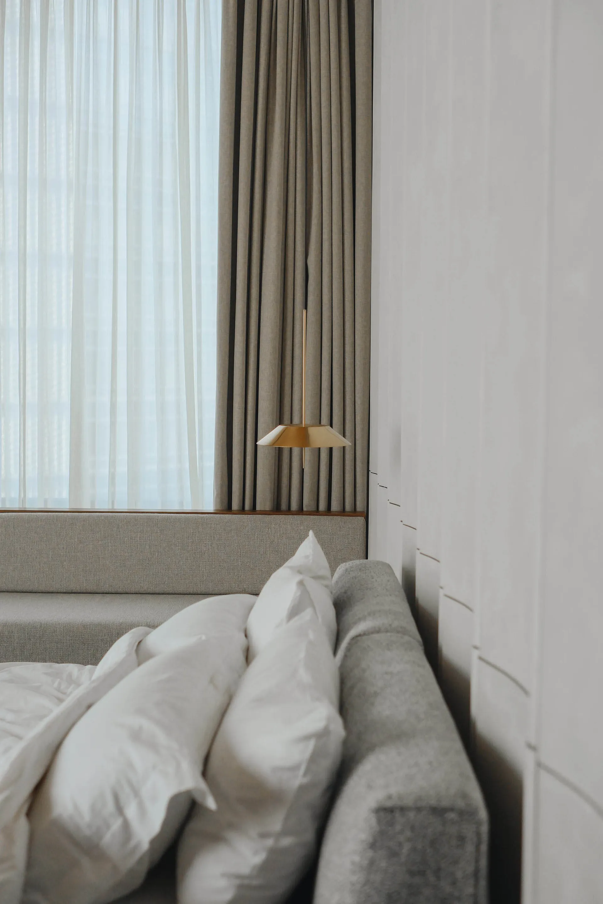 A minimalist grey bedroom with textile curtains and a fabric headboard.