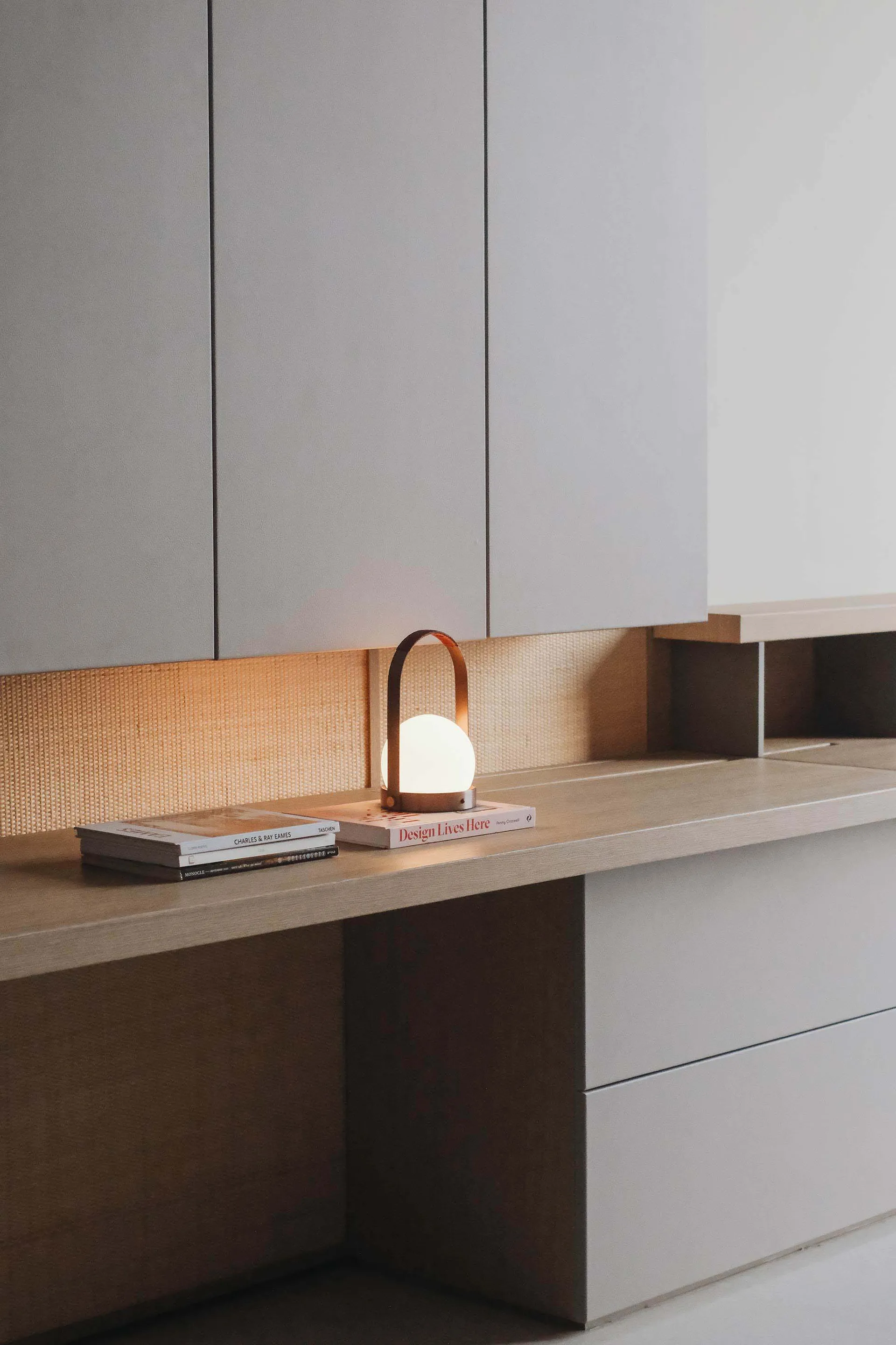 A minimalist interior design space featuring a wooden counter with books, a light lamp, and organized shelves.