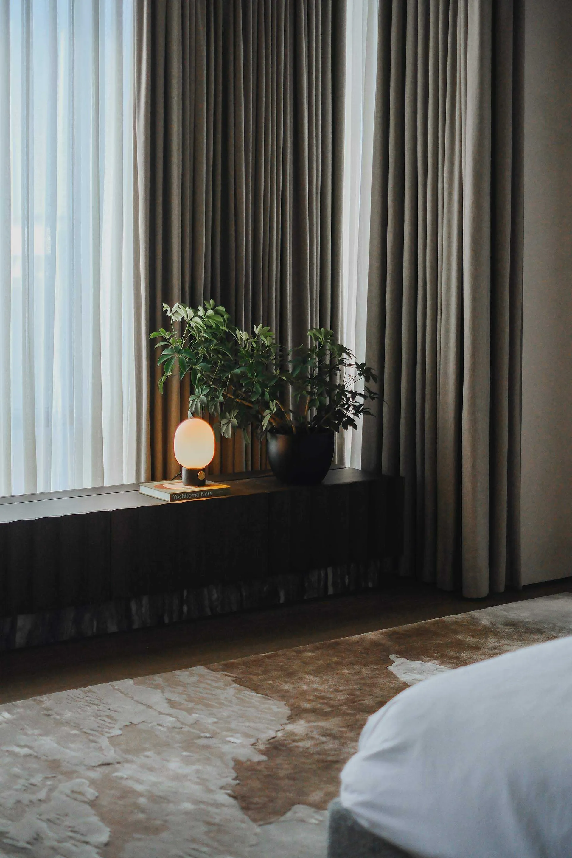 Modern minimalist bedroom featuring fabric curtains, a reading lamp, and a plant on a floating nightstand.