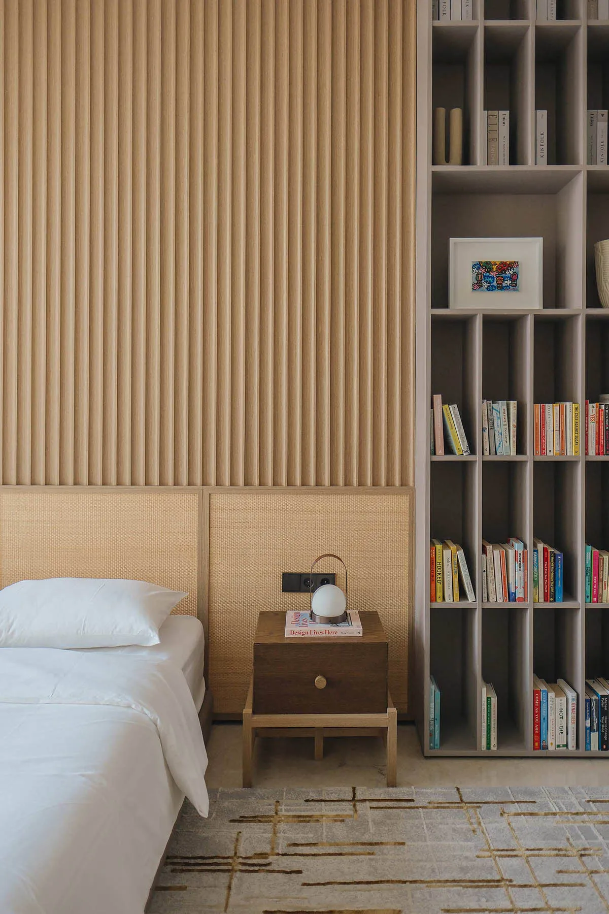 A modern minimalist bedroom featuring a bed with a wooden headboard, a wooden nightstand, and a large bookshelf filled with b
