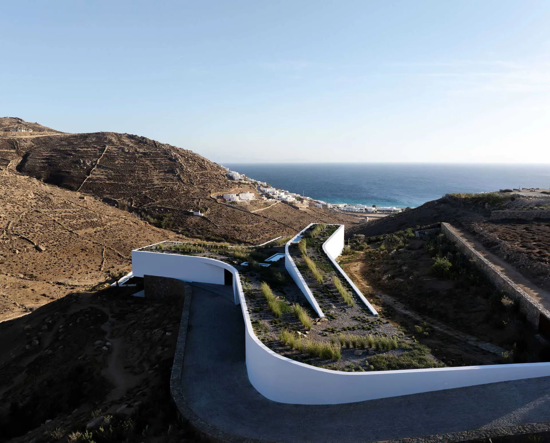A modern minimalist building with a concrete roof and garden overlooking a coastal landscape.