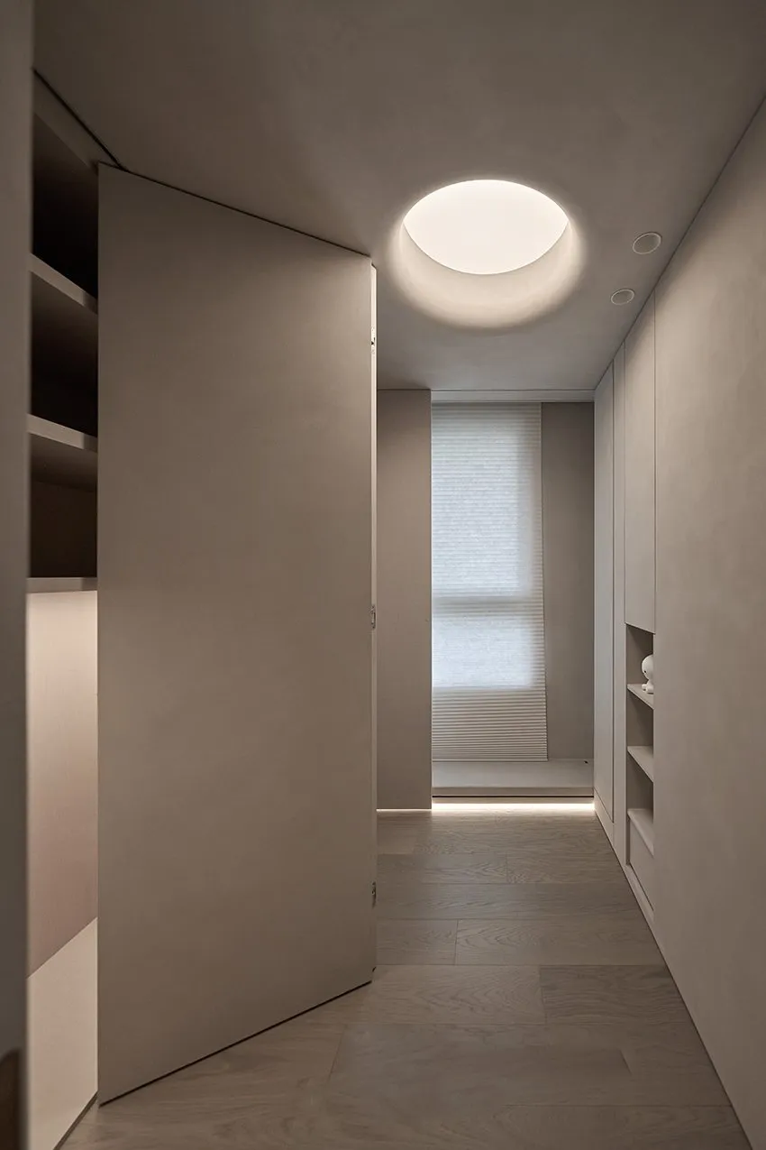 Modern minimalist corridor with concrete walls, wooden floor, and large circular light fixture.