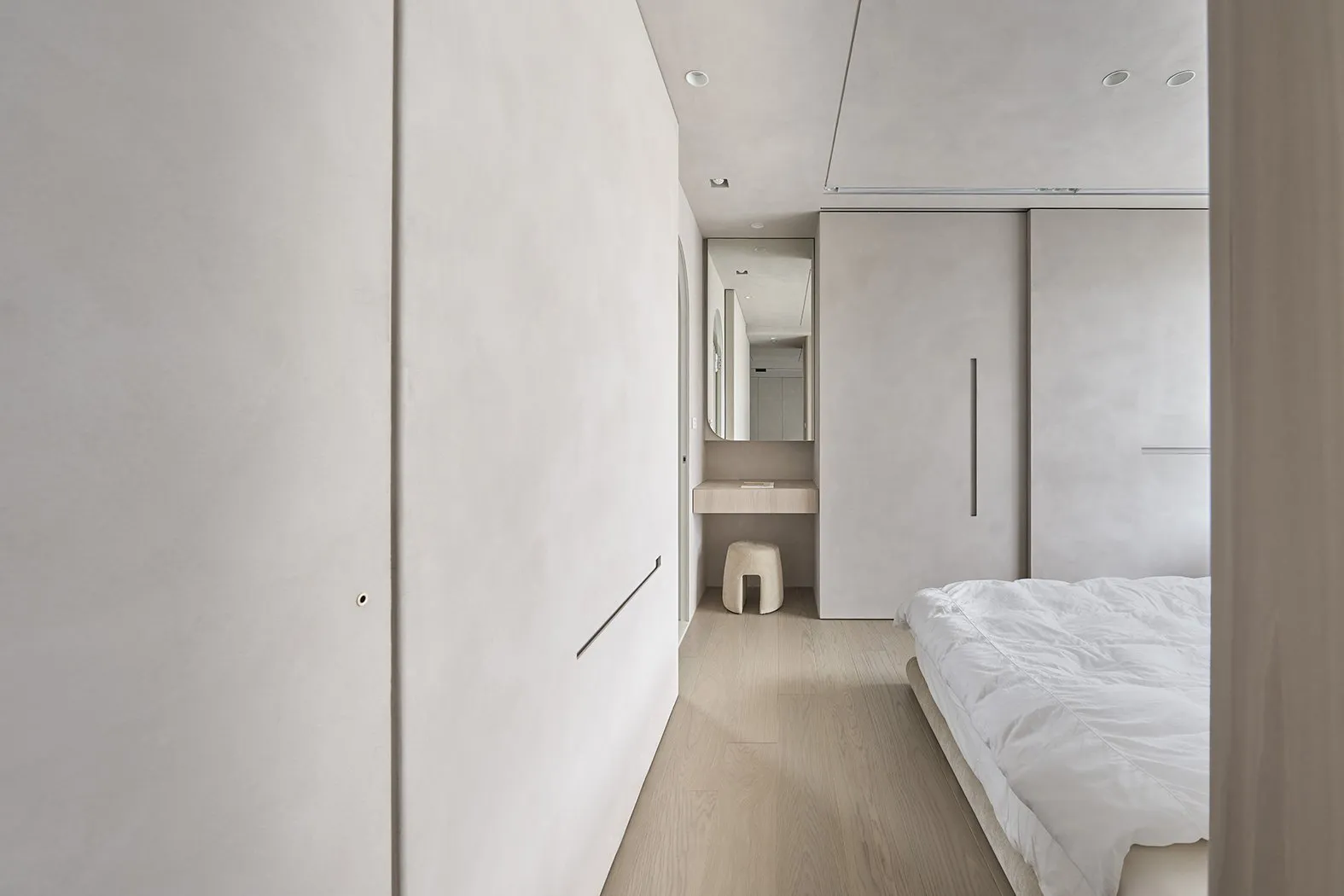 A contemporary minimalist bedroom featuring concrete walls, natural wood flooring, and simple white furniture.