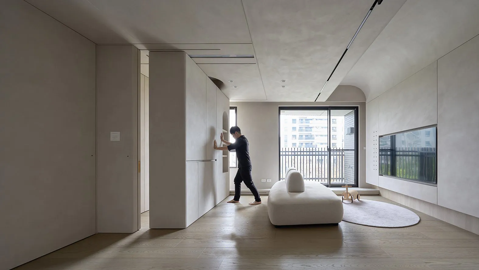 A minimalist living room featuring a white sofa and concrete floors and walls.