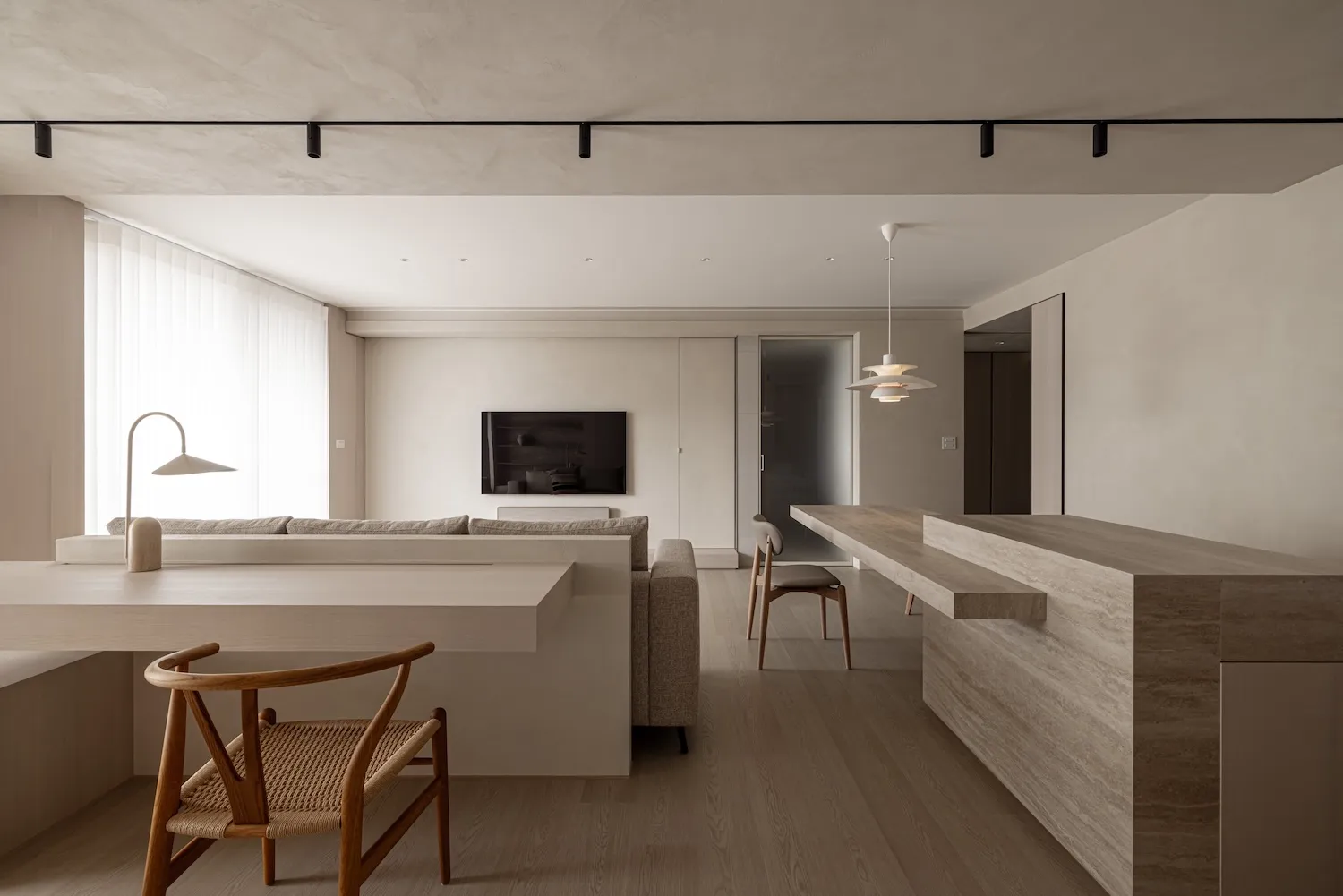 A modern minimalist living room with concrete finishes, a flat-screen TV, and a dining area with a wooden table and chairs.
