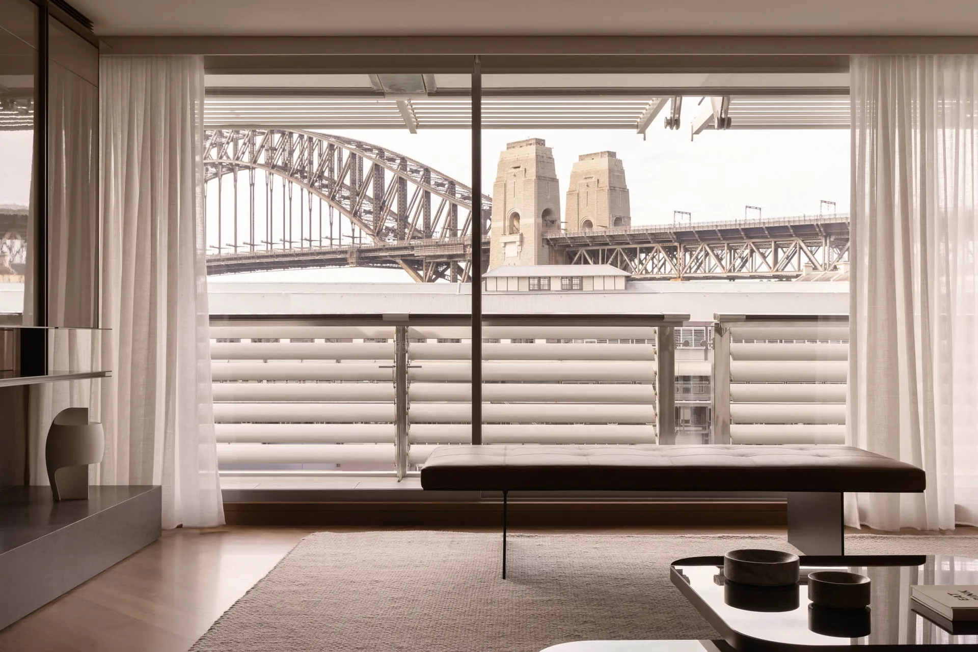 A contemporary living room showcasing minimalist design features, with a view of the Sydney Harbour Bridge and iconic towers