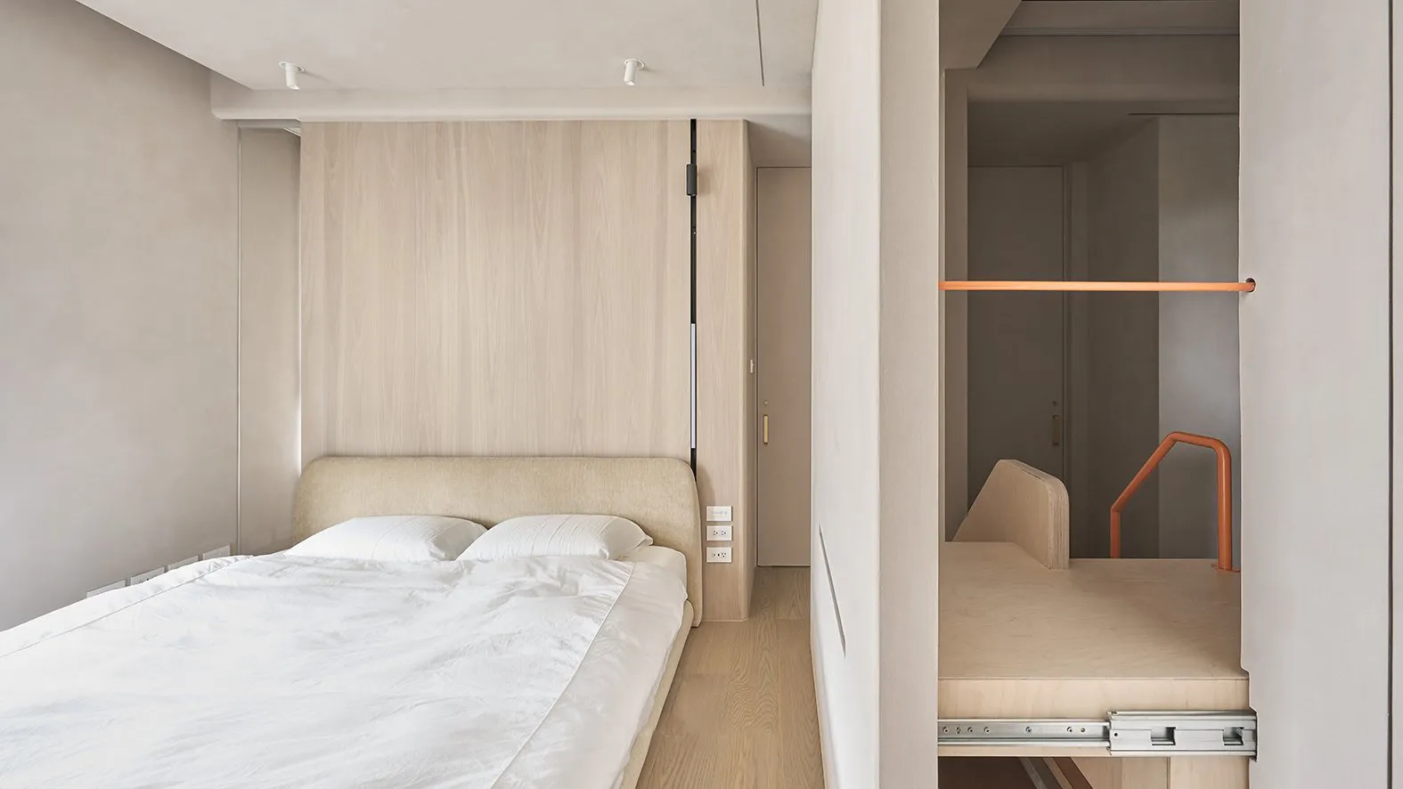 A modern minimalist bedroom with a bed against the wall and a pull-out storage unit.