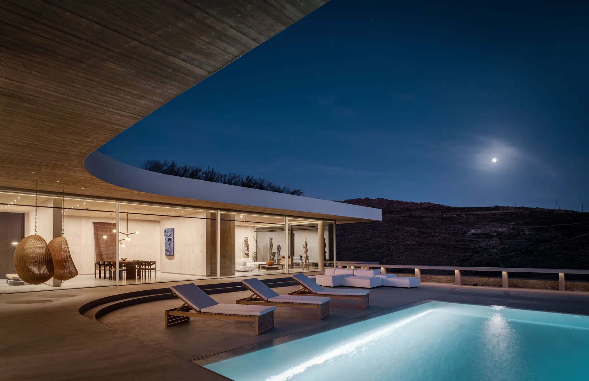 Modern residential space featuring concrete and glass materials, with a pool and lounge area.