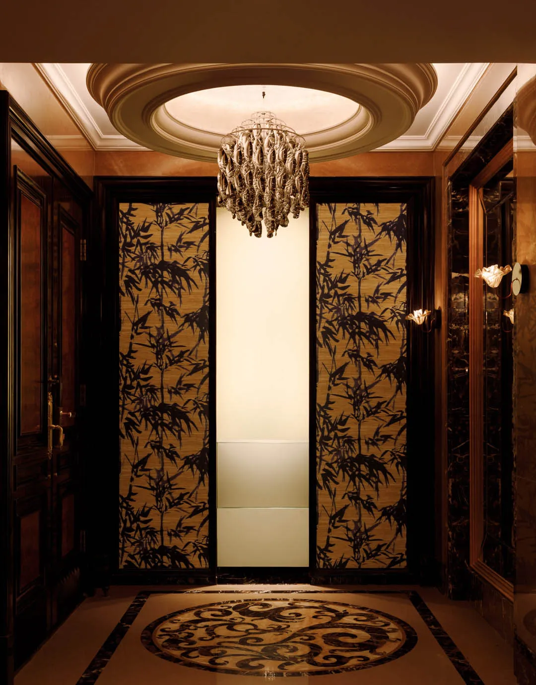 A luxurious entrance area featuring elegant elevators enclosed in glass and framed by rich, wooden elements.