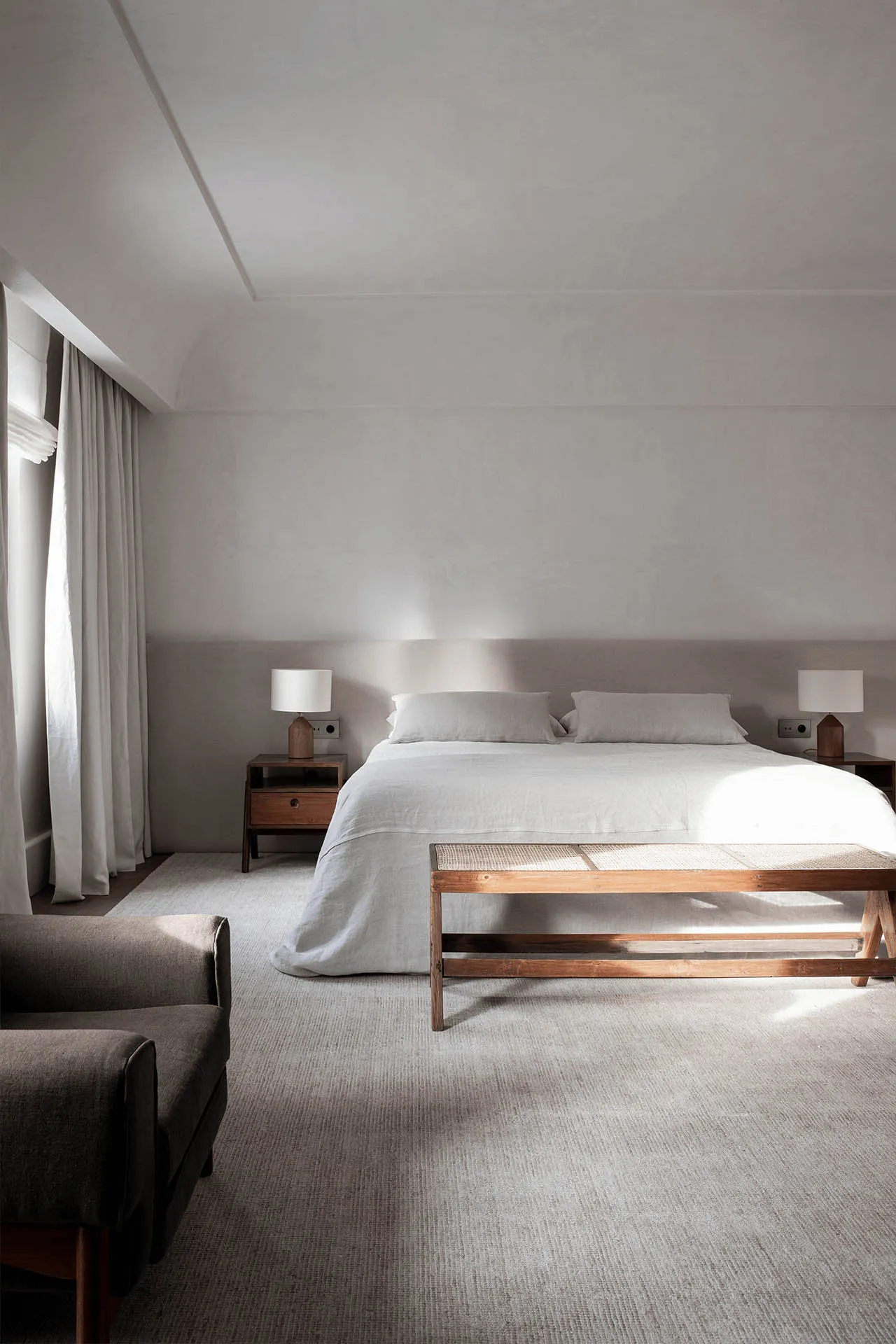 A minimalist bedroom featuring a large bed with linen bedding and wooden furniture.