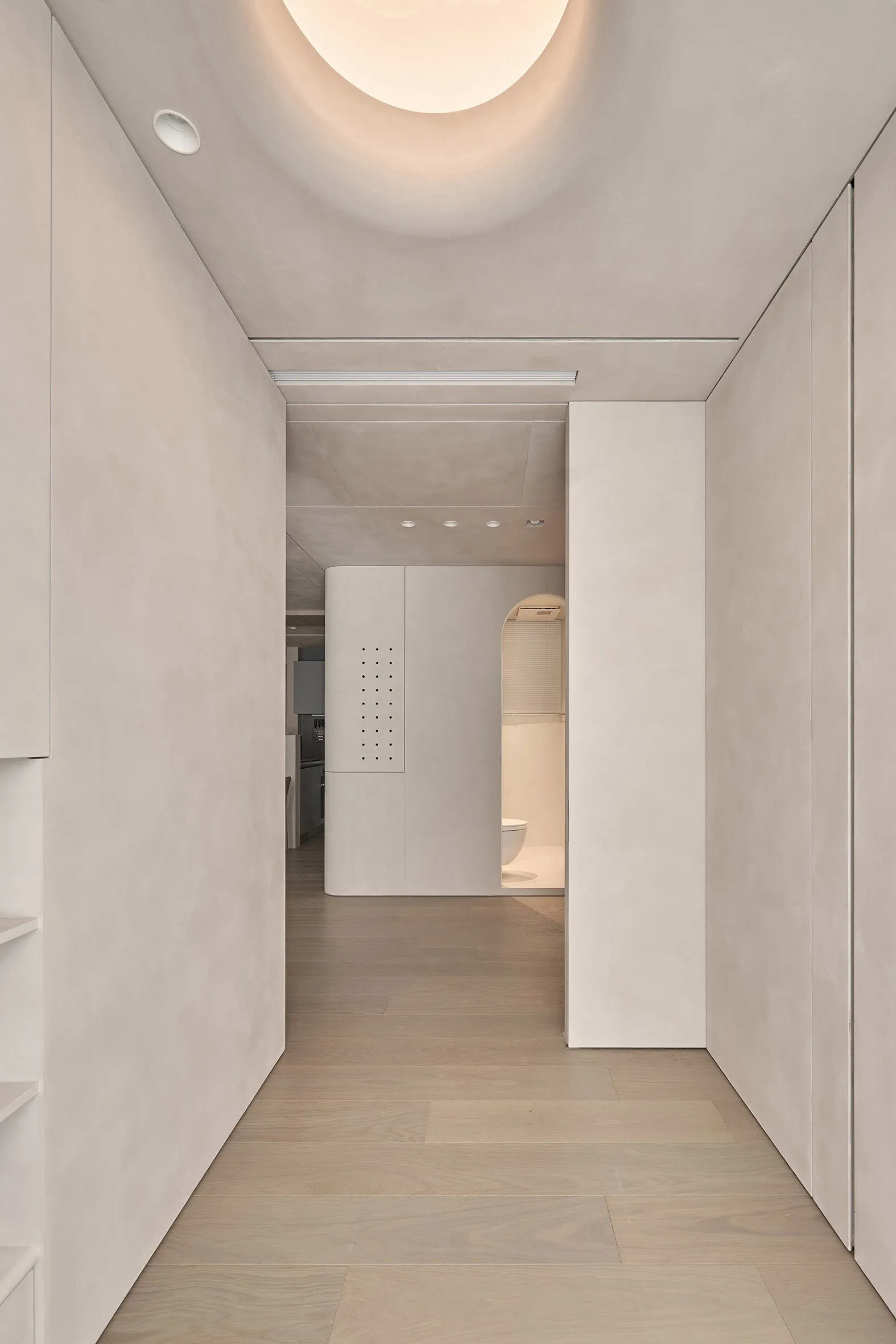 A minimalist corridor with light-colored plaster walls and wooden flooring.