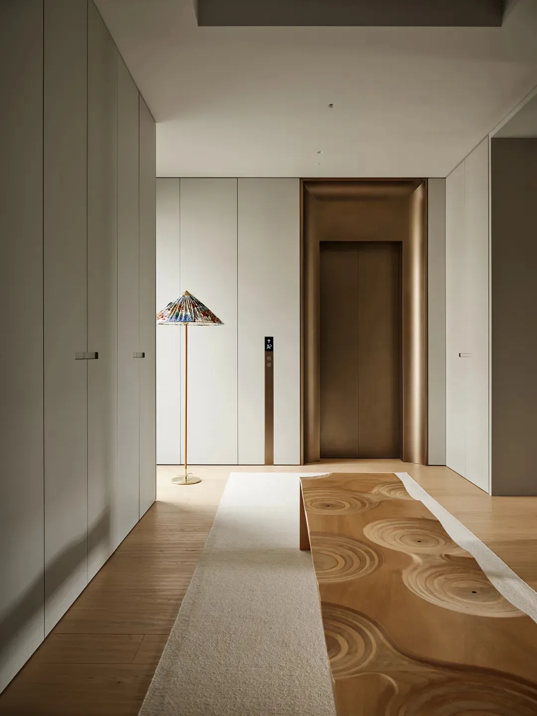 A modern corridor featuring wooden flooring and a patterned wooden bench with a colorful umbrella lamp.