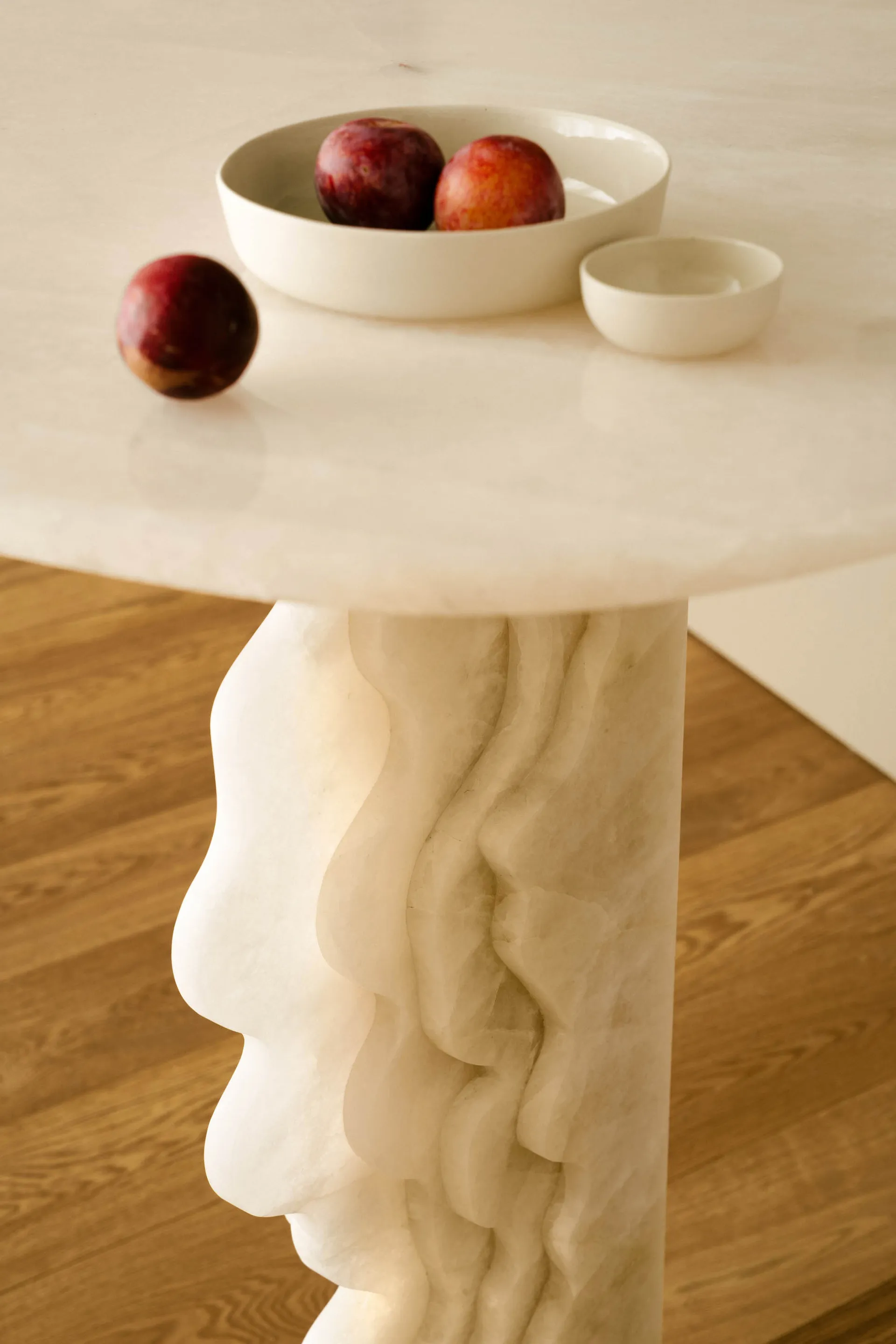 A modern side table made of marble with a sculptural, organic design, featuring a bowl of red plums and a single plum on the 