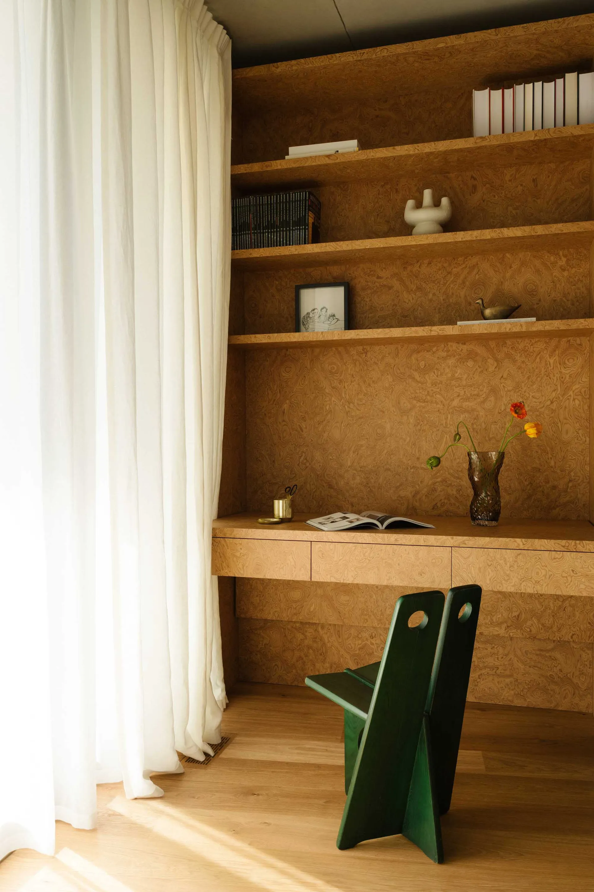 A modern, minimalist home office with wooden furniture, white curtains, and a green chair.