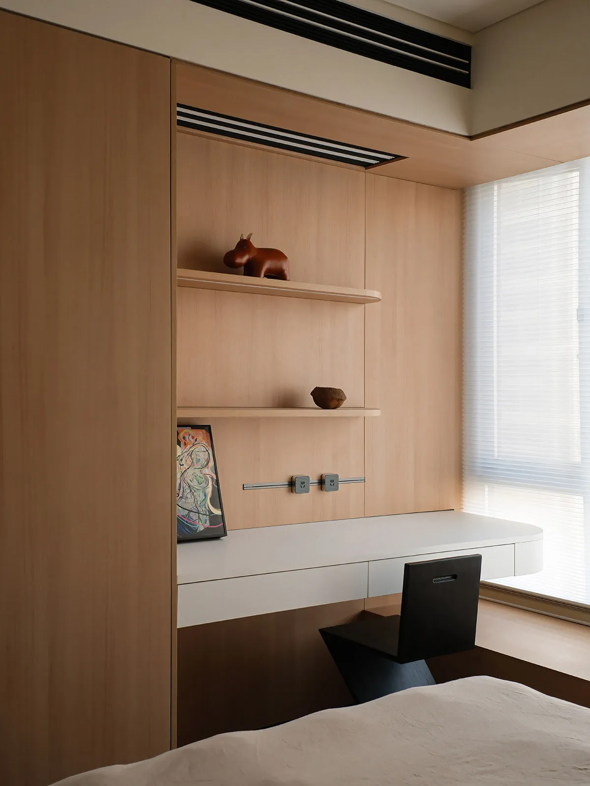 A minimalist desk space featuring a wooden desk and shelf with decorative items and a black chair.