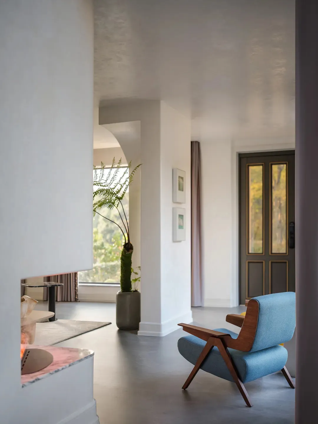 A modern minimalist living room with a concrete floor, blue armchair, and large windows.