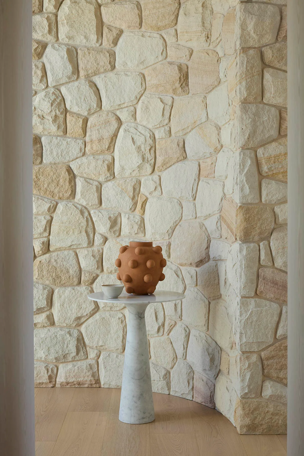 A modern entryway featuring a stone floor and a concrete table with a unique vase on it.