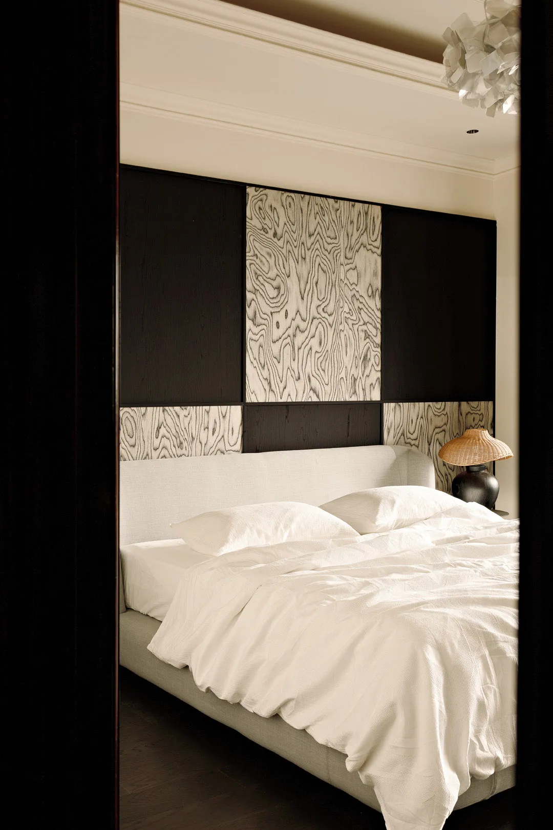 A modern minimalist bedroom featuring a white upholstered bed with a simple headboard, placed against a wall with dark and li