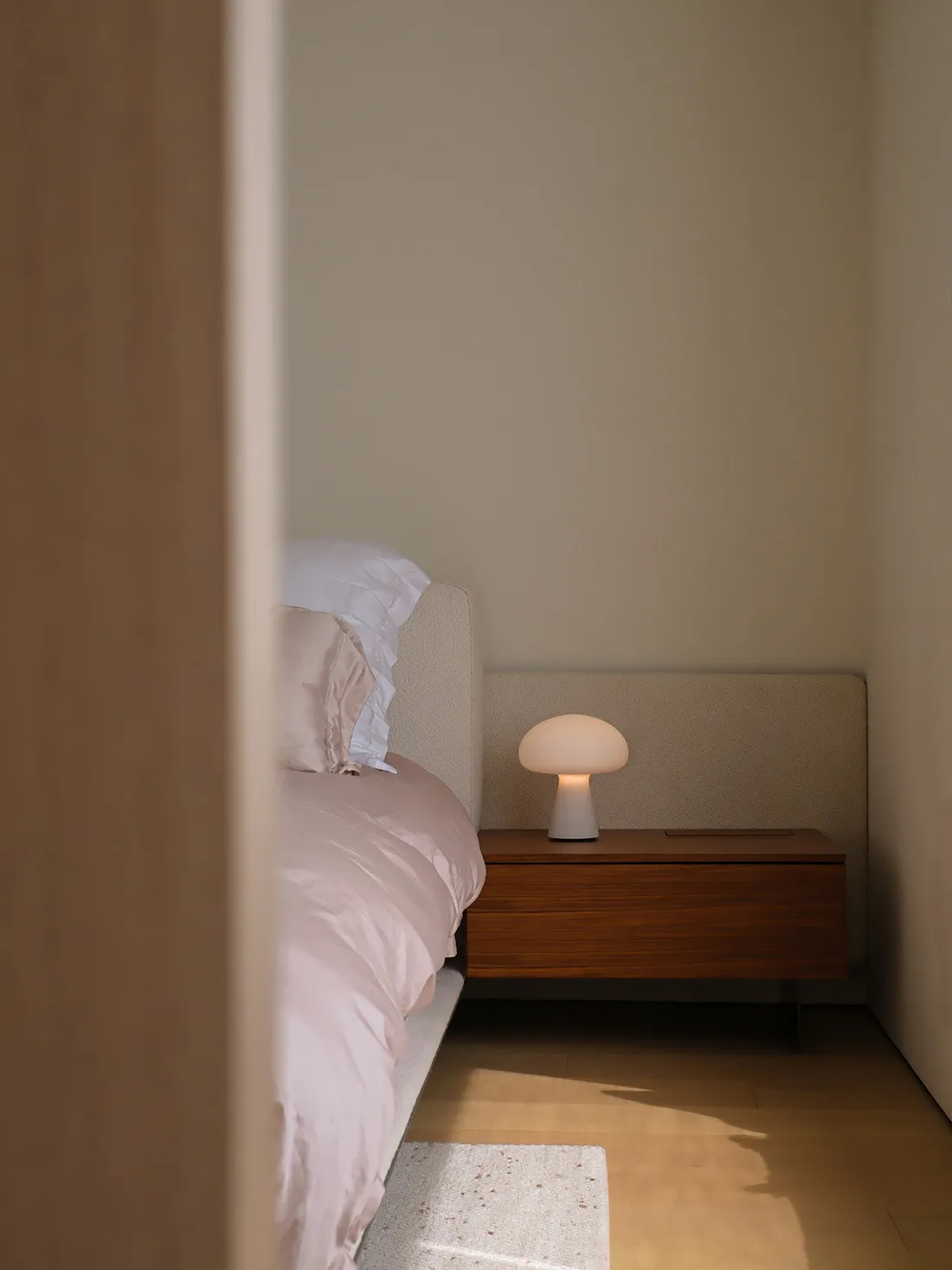 Modern minimalist bedroom featuring a bed with white bedding and a white mushroom-shaped lamp on a floating nightstand.