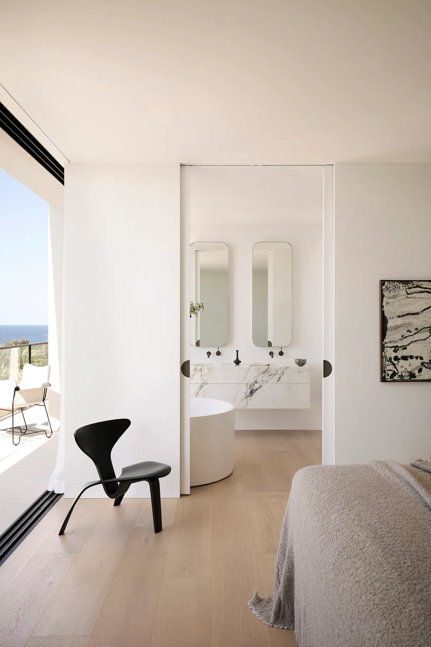 A modern residential interior featuring a marble bathroom with a round bathtub, double vanity, and floor-to-ceiling windows.