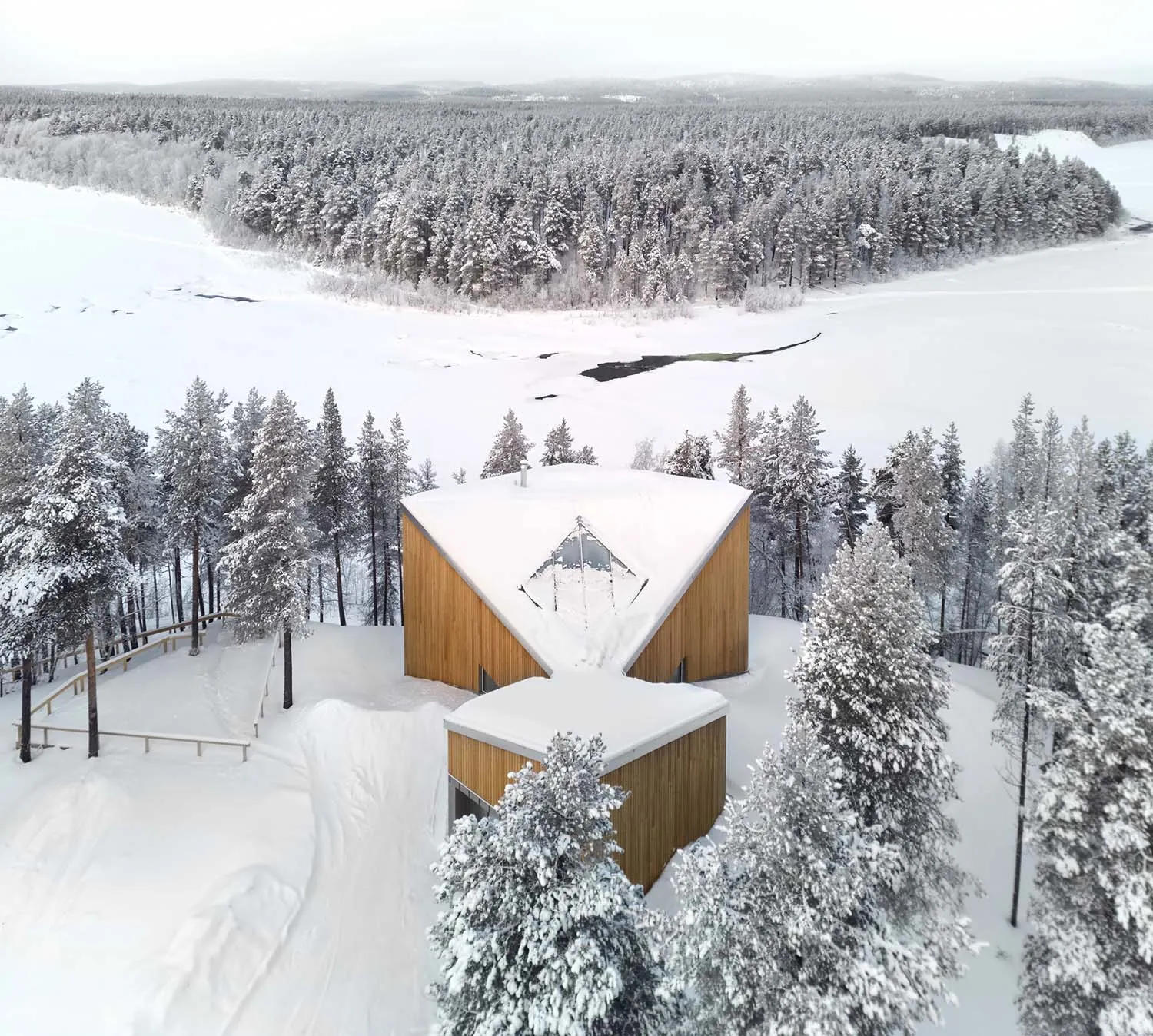 A modern winter cabin covered in snow with a wooden exterior.