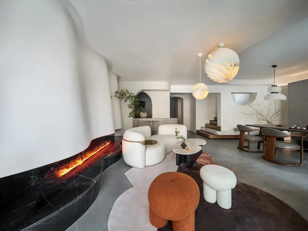 A modern living room with a fire pit, curved couch, and round ottoman.