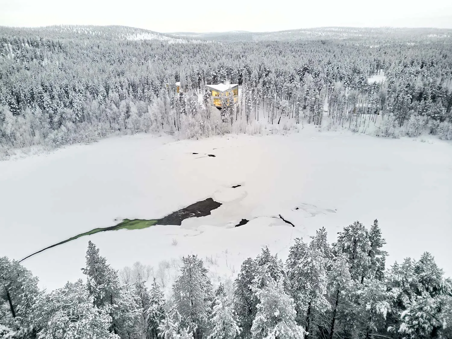 Aerial view of a snow-covered residential house nestled in a frozen forest.