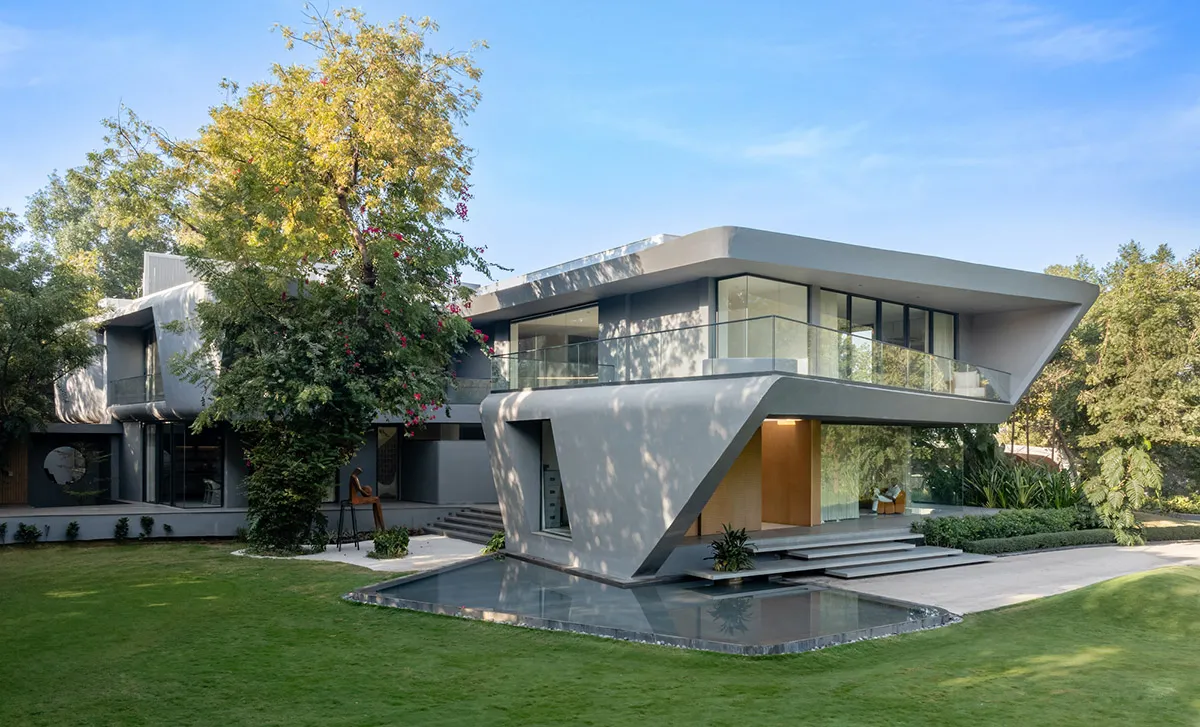 A modern, minimalist house with a concrete exterior and large glass windows, surrounded by greenery.
