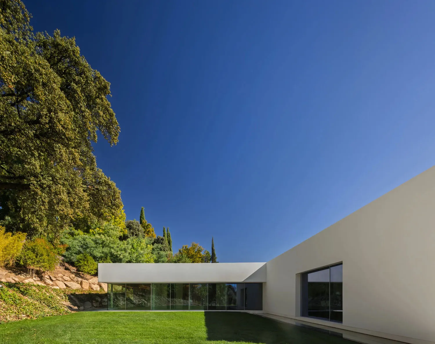 A modern minimalist house featuring a concrete exterior and glass walls.