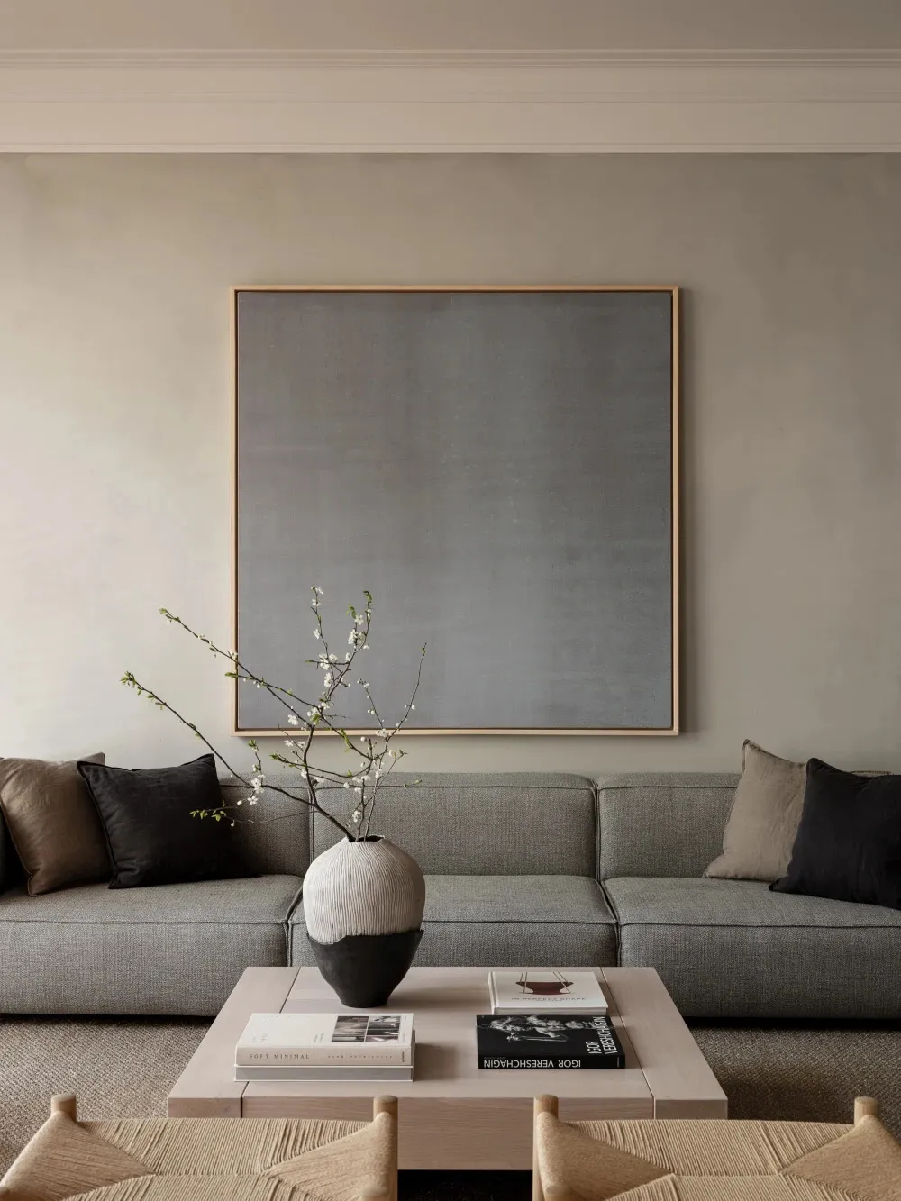 A modern monochromatic living room featuring a textured fabric sofa and a minimalist vase with white blossoms on a coffee tab