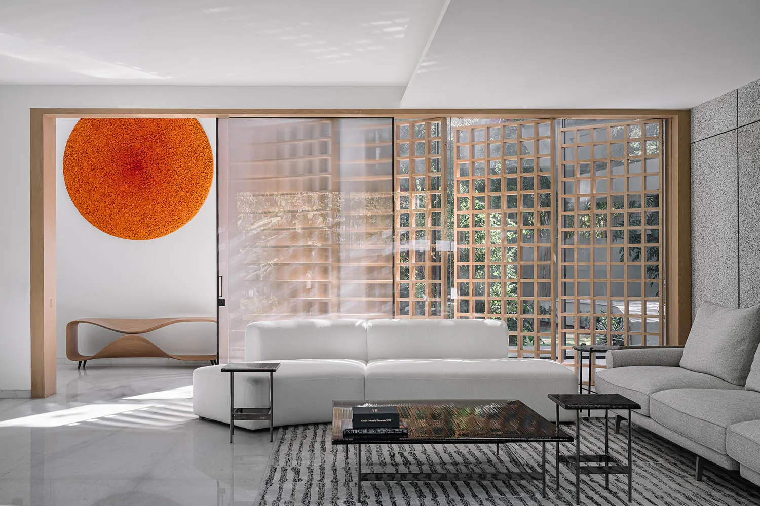 A modern living room with concrete walls, minimalist furniture, and a large, round orange artwork hanging on the wall.