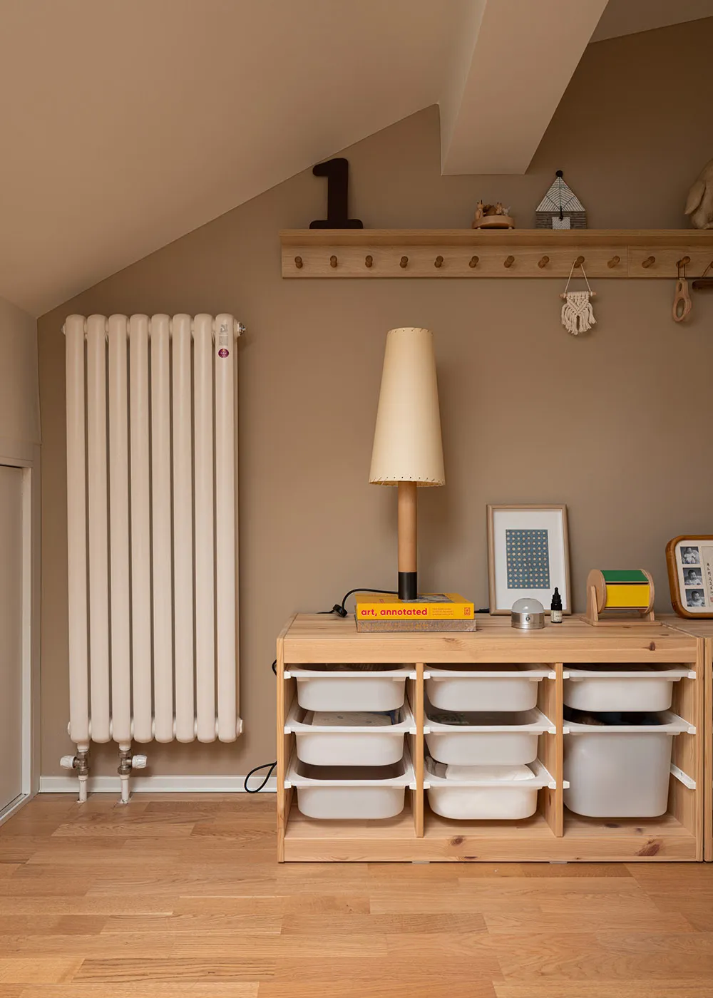 A modern interior design featuring a wood storage unit with white bins and a lamp on top, with a radiator and coat rack in th
